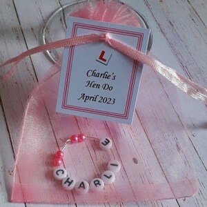 May include: Pink organza bag with a white card that says "Charlie's Hen Do April 2023" and a pink and white letter charm inside the bag