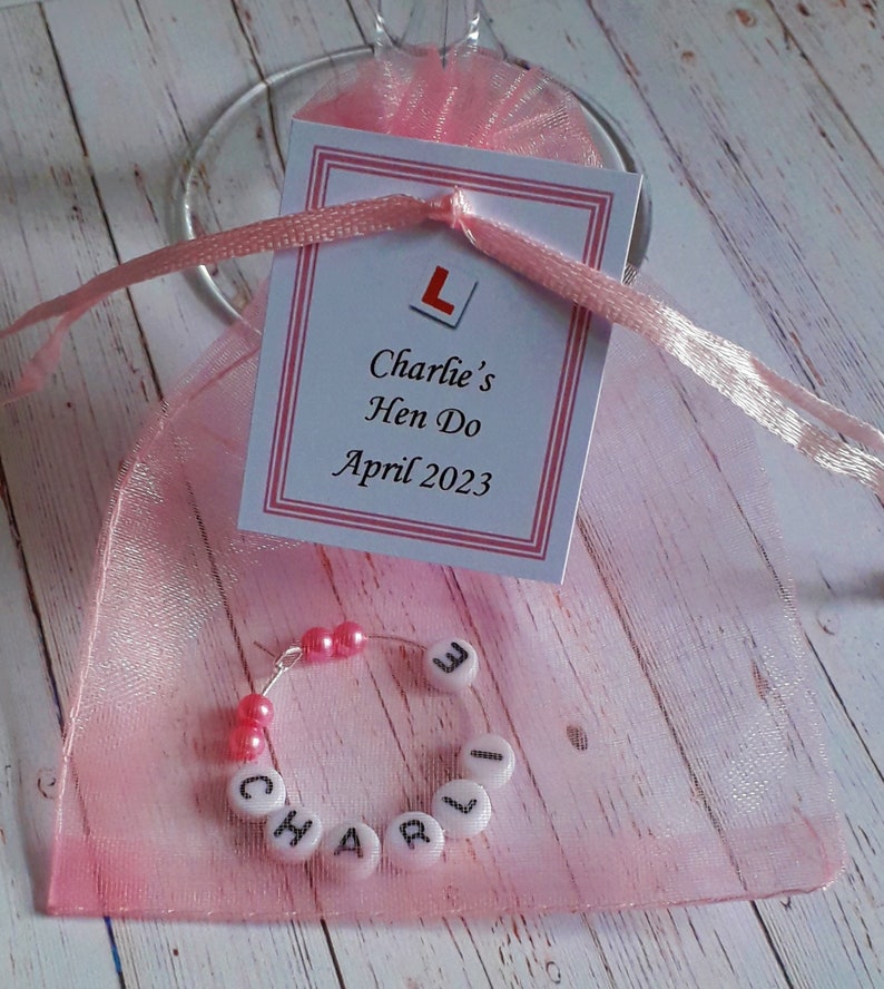 May include: Pink organza bag with a white card that says "Charlie's Hen Do April 2023" and a pink and white letter charm inside the bag
