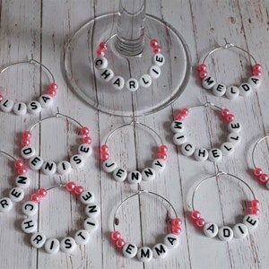 May include: wine glass charms with pink beads and white letters spelling out names,