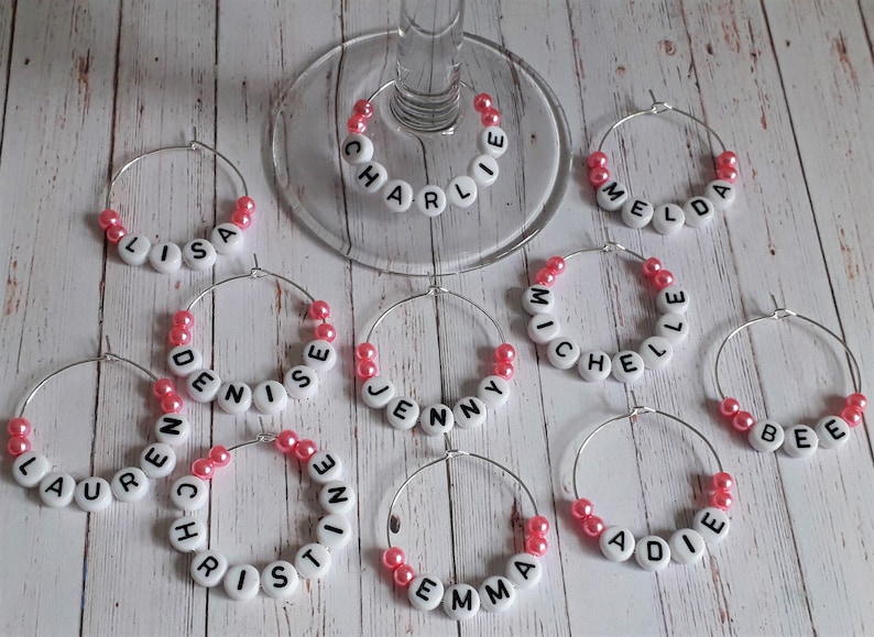 May include: wine glass charms with pink beads and white letters spelling out names,