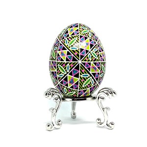 May include: A hand-painted Easter egg with a geometric design in shades of pink, green, and black. The egg is displayed on a silver stand.