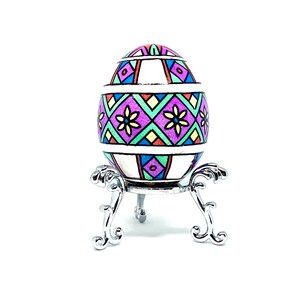 May include: A colorful, geometrically patterned Easter egg on a silver stand. The egg is decorated with pink, purple, green, blue, yellow, and red.