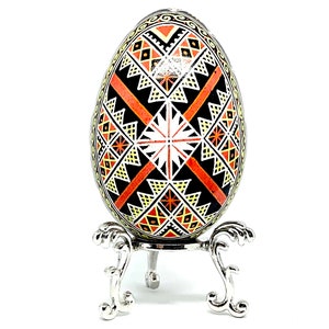 May include: A black egg with a geometric pattern in orange, white, and yellow colors is displayed on a silver stand. The egg is decorated with a traditional folk art design.