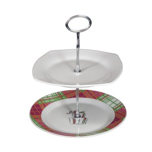 Op de afbeelding: Een tweelaagse witte keramische serveerstandaard met een zilveren metalen standaard. De onderste laag heeft een roze, groene en oranje geruite ontwerp met een witte cadeaudoos illustratie. De bovenste laag is een eenvoudige witte vierkante plaat.
