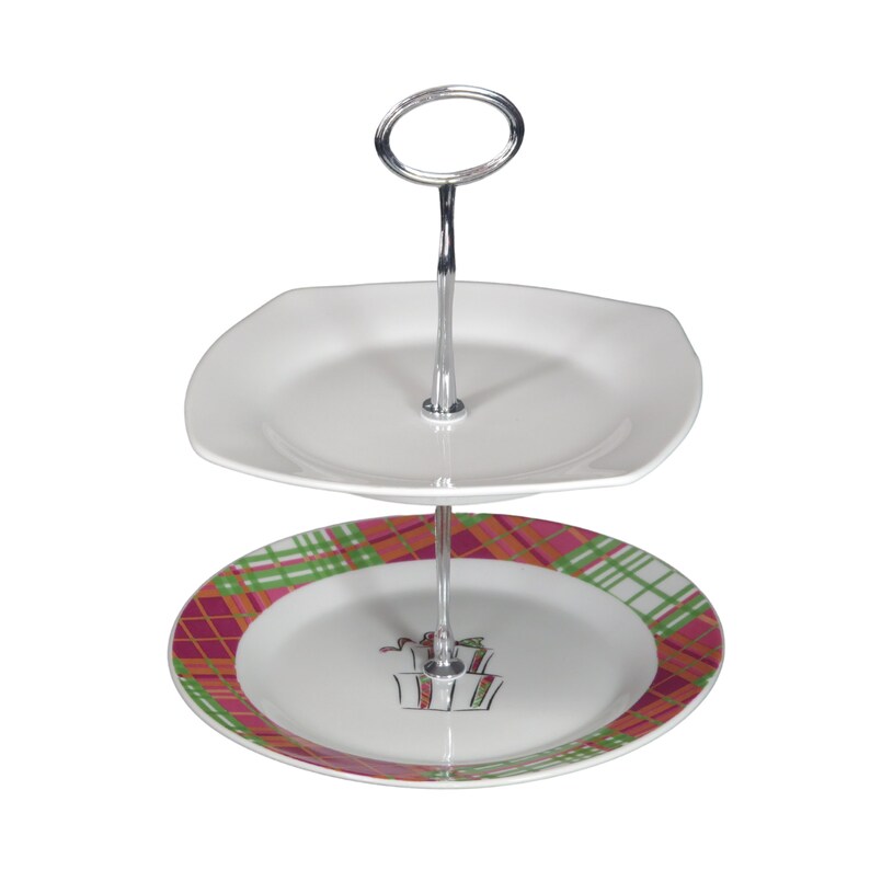 Op de afbeelding: Een tweelaagse witte keramische serveerstandaard met een zilveren metalen standaard. De onderste laag heeft een roze, groene en oranje geruite ontwerp met een witte cadeaudoos illustratie. De bovenste laag is een eenvoudige witte vierkante plaat.