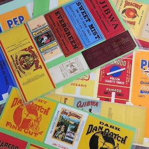May include: A collection of vintage tobacco labels in various colors, including yellow, red, and blue. The labels feature text such as "Sweet Mist," "Evergreen," and "Dan Patch Fine Cut." The labels are arranged on a green background.