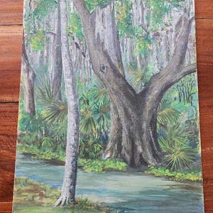 May include: An acrylic painting of a swamp scene. The artwork depicts a tranquil waterway surrounded by lush greenery, including palm trees and Spanish moss. The painting features a large, textured tree trunk and a serene, light blue water.