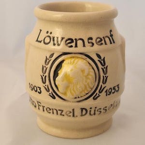 May include: A ceramic mustard jar with a lion head design and the text "LöwenSenf 1903 - 1953 Otto Frenzel. Düsseldor" in black lettering.