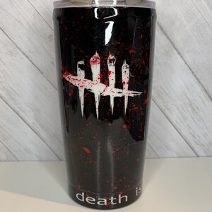 Può includere: Bicchiere nero con un design a spruzzi bianchi e rossi. Il bicchiere presenta una grafica bianca di quattro linee verticali incrociate da una linea orizzontale, con le parole "death is" in basso.