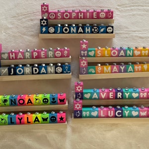 Puede incluir: Un conjunto de ocho menor&aacute;s de madera de colores, cada una con un nombre diferente escrito en la parte delantera. Los nombres son: Sophie, Jonah, Harper, Jordan, Sloan, Maya, Avery y Lucy. Cada menor&aacute; tiene una variedad de peque&ntilde;os s&iacute;mbolos en los bloques, incluyendo estrellas, corazones, arco&iacute;ris y mariposas.
