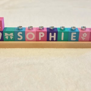 Puede incluir: Una menor&aacute; de madera con bloques coloridos que deletrean el nombre "SOPHIE". Los bloques tienen diferentes dise&ntilde;os, incluyendo una estrella de David, un coraz&oacute;n, un lazo, una flor y un coraz&oacute;n.