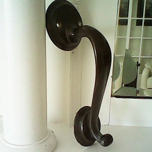 May include: A black metal door handle with a curved lever and a round base. The handle is attached to a white surface.