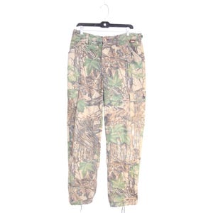 May include: Cargo pants featuring a realistic forest camouflage pattern in shades of tan, brown, and green. The pants include side cargo pockets with button closures, a front button and zipper fly, belt loops, and adjustable drawstrings at the hem.