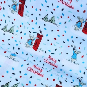 Puede incluir: Tela blanca con un patrón repetido de un conejo entregando correo a un buzón rojo. La tela tiene un tema navideño festivo con las palabras "Feliz Navidad" y "Alegría" repetidas en todo el patrón.