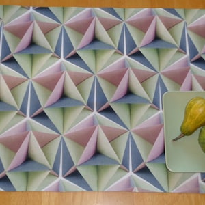 Könnte beinhalten: Ein geometrischer Tischläufer mit einem sich wiederholenden Muster aus rosa, grünen und blauen Dreiecken. Der Läufer liegt auf einer Holzoberfläche und ein grüner Teller mit zwei Kürbissen liegt auf dem Läufer.