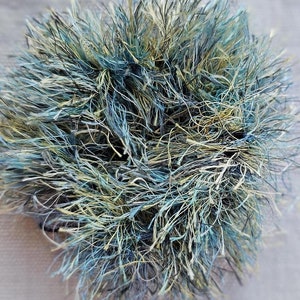 May include: A ball of yarn in shades of blue, green, and beige. The yarn is very fluffy and has a soft texture.
