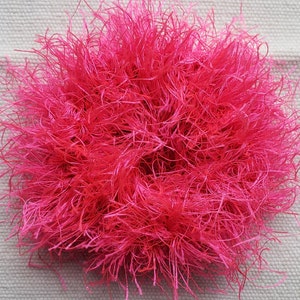 May include: A bright pink fluffy hair scrunchie made of yarn.