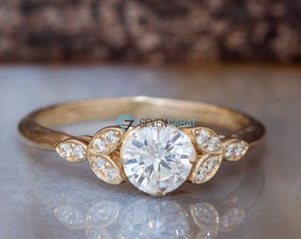 May include: A gold engagement ring featuring a round centre stone and smaller stones set in leaf-shaped accents.