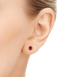 以下が含まれることがあります： ルビーのスタッドピアスのペア。ピアスは小さく丸く、シルバーのセッティングにセットされています。