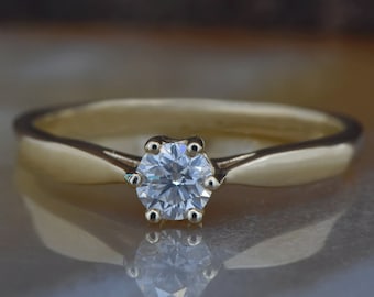 May include: A gold band engagement ring with a single round diamond.
