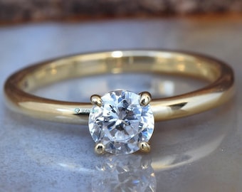 May include: A simple gold band ring with a single round, clear gemstone.