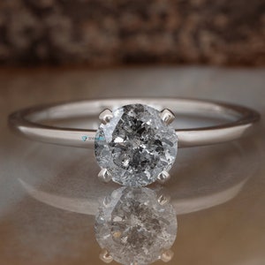 Puede incluir: Un anillo de compromiso de plata con un diamante redondo gris.