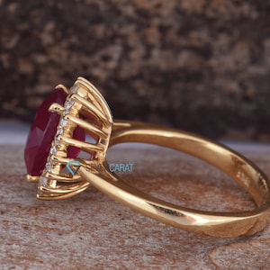 Puede incluir: Un anillo de oro con un gran rub&iacute; de forma ovalada rodeado por un halo de diamantes m&aacute;s peque&ntilde;os. El anillo est&aacute; engastado en un estilo cl&aacute;sico con una banda lisa.