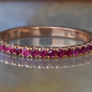 Könnte beinhalten: Ein Roségold-Bandring mit einer Reihe kleiner, leuchtend roter Rubin-Steine, die in die Band gefasst sind.