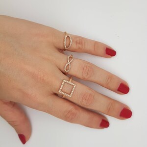 May include: Three gold rings with clear stones. The rings are in the shape of a square, an infinity symbol, and an oval.