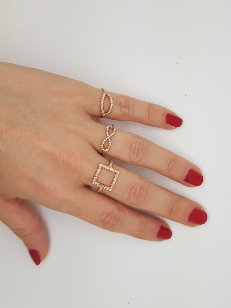 May include: Three gold rings with clear stones. The rings are in the shape of a square, an infinity symbol, and an oval.