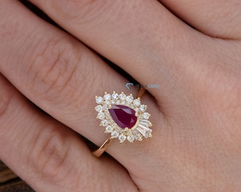 Op de afbeelding: Een gouden ring met een peervormige robijn, omringd door kleinere diamanten. De ring is gezet in een delicaat, bloemig geïnspireerd ontwerp.