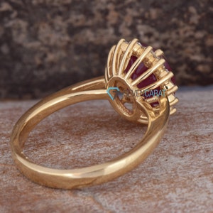 Puede incluir: Un anillo de oro con una gran piedra roja rodeada de diamantes m&aacute;s peque&ntilde;os. El anillo est&aacute; engastado en un estilo halo con una banda delicada.