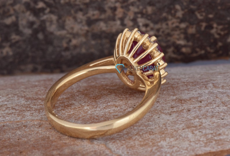 Puede incluir: Un anillo de oro con una gran piedra roja rodeada de diamantes m&aacute;s peque&ntilde;os. El anillo est&aacute; engastado en un estilo halo con una banda delicada.