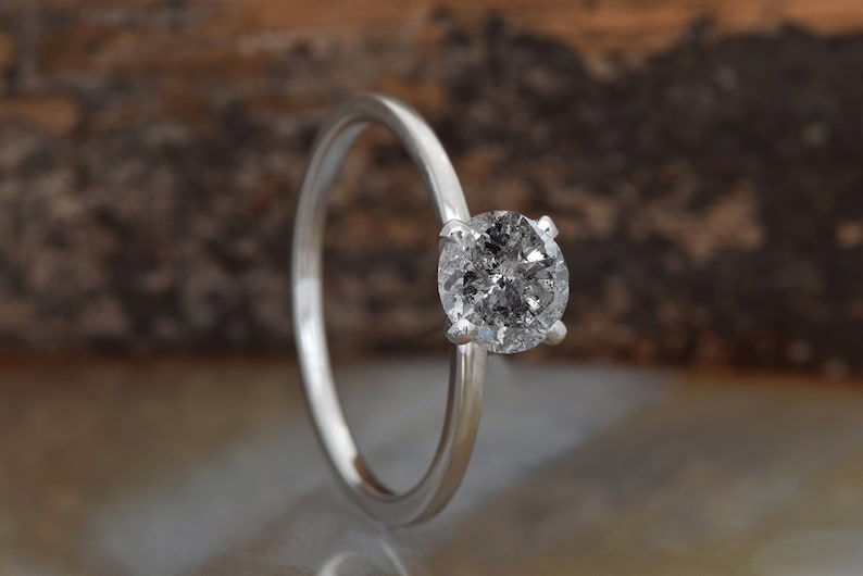 Puede incluir: Un anillo de compromiso solitario de plata con un diamante redondo gris.