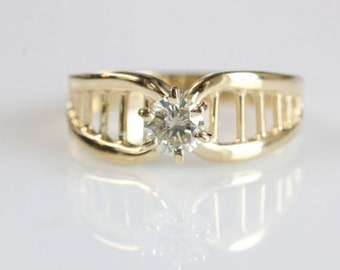 Op de afbeelding: Een gouden ring met een diamant in een kooivormig ontwerp.
