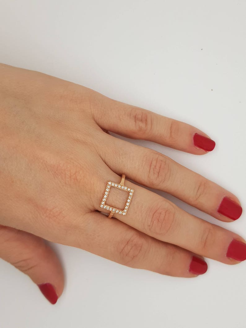 May include: A gold ring with a square-shaped setting of small clear stones.