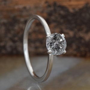 Puede incluir: Un anillo de compromiso de plata con un diamante redondo gris.