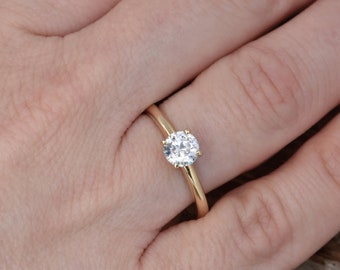 May include: A gold band engagement ring with a round, clear diamond.