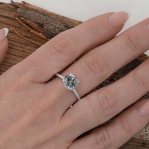Puede incluir: Un anillo de compromiso de plata con un gran diamante redondo gris.