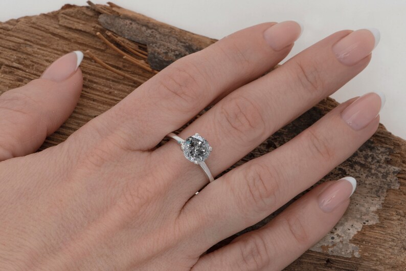 Puede incluir: Un anillo de compromiso de plata con un gran diamante redondo gris.