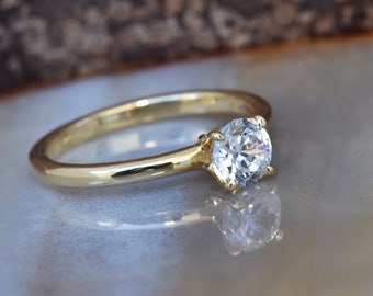 May include: A simple gold band ring with a single round clear gemstone.
