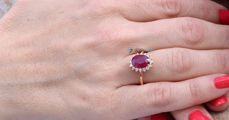 Puede incluir: Un anillo de oro con un gran rub&iacute; ovalado rodeado de diamantes m&aacute;s peque&ntilde;os.