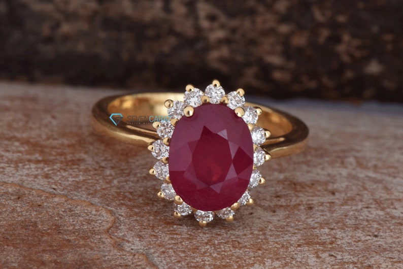 Puede incluir: Un anillo de oro con un gran rub&iacute; ovalado rodeado por un halo de diamantes m&aacute;s peque&ntilde;os.