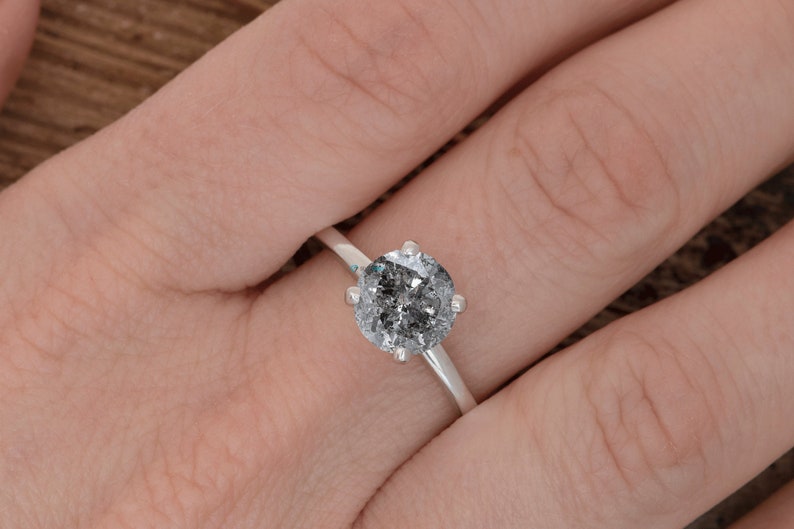 Puede incluir: Un anillo de compromiso de plata con un gran diamante redondo gris.