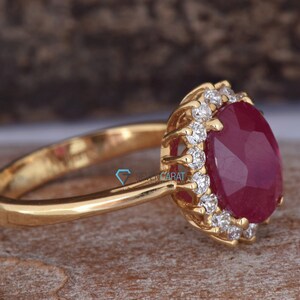 Puede incluir: Un anillo de oro con una gran piedra de rub&iacute; ovalada rodeada de diamantes m&aacute;s peque&ntilde;os. El anillo est&aacute; engastado en un estilo halo.
