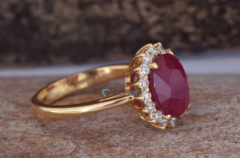 Puede incluir: Un anillo de oro con una gran piedra de rub&iacute; ovalada rodeada de diamantes m&aacute;s peque&ntilde;os. El anillo est&aacute; engastado en un estilo halo.