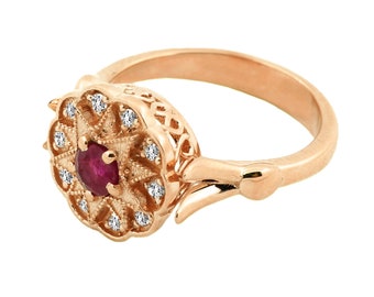 May include: A rose gold ring with a ruby gemstone surrounded by a halo of smaller diamonds. The ring has a delicate, intricate design.