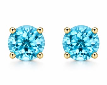 May include: A pair of round-cut, bright blue gemstone stud earrings set in polished yellow gold. Each stone is secured by four small, rounded prongs that hold the circular gems firmly in place, creating a classic and symmetrical jewelry design.
