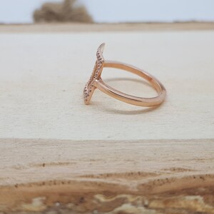 May include: A rose gold ring with a geometric design. The ring is set with small, clear stones.