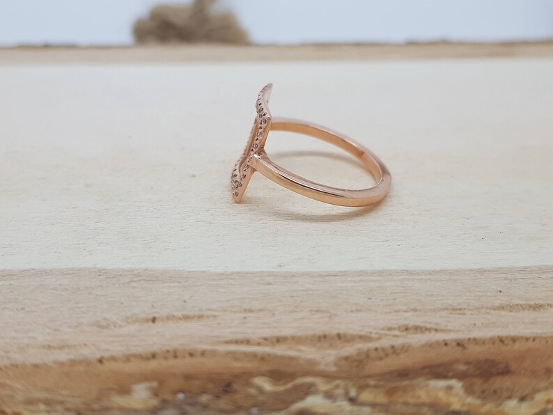 May include: A rose gold ring with a geometric design. The ring is set with small, clear stones.